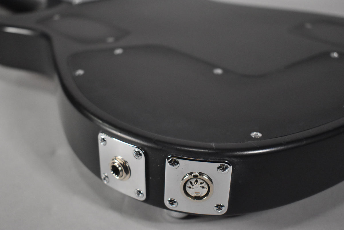 Close-up of the guitar's lower bout, showing the matte black finish, a chrome 1/4" jack, and a chrome 7-pin MIDI output.