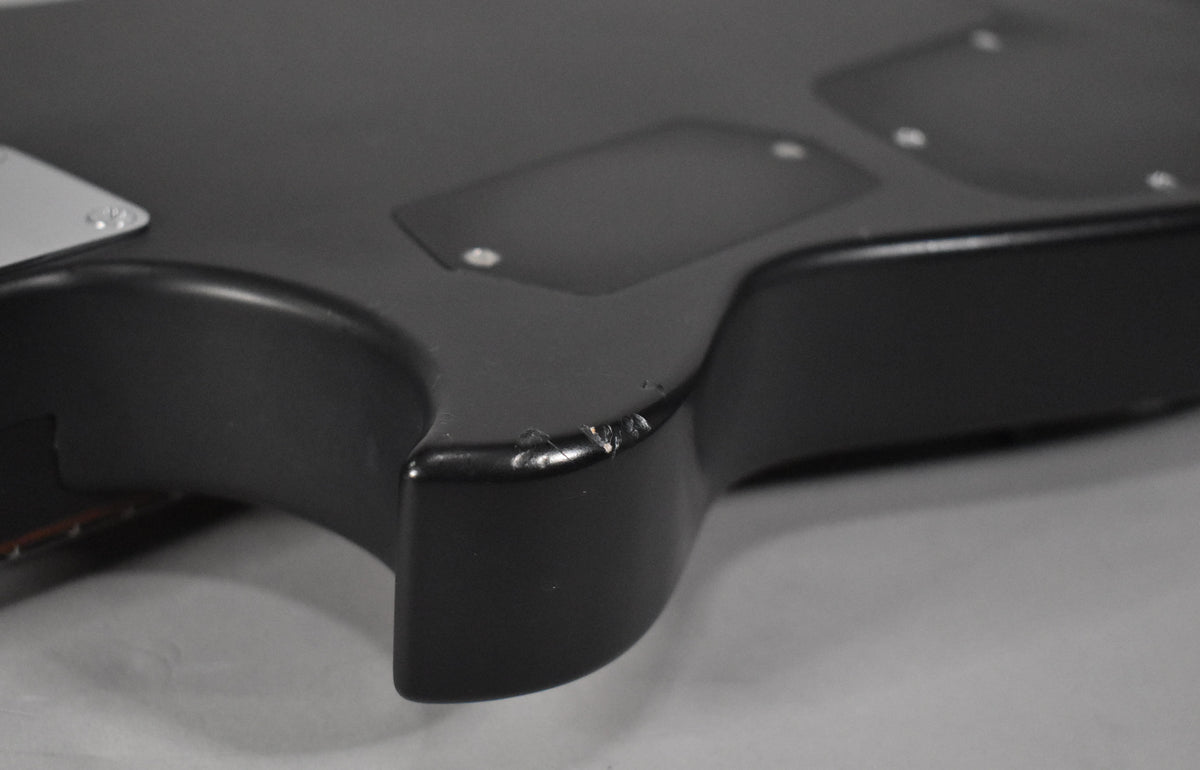 Close-up of the guitar's lower body, showing a matte black finish with several chips and scratches on the edge.