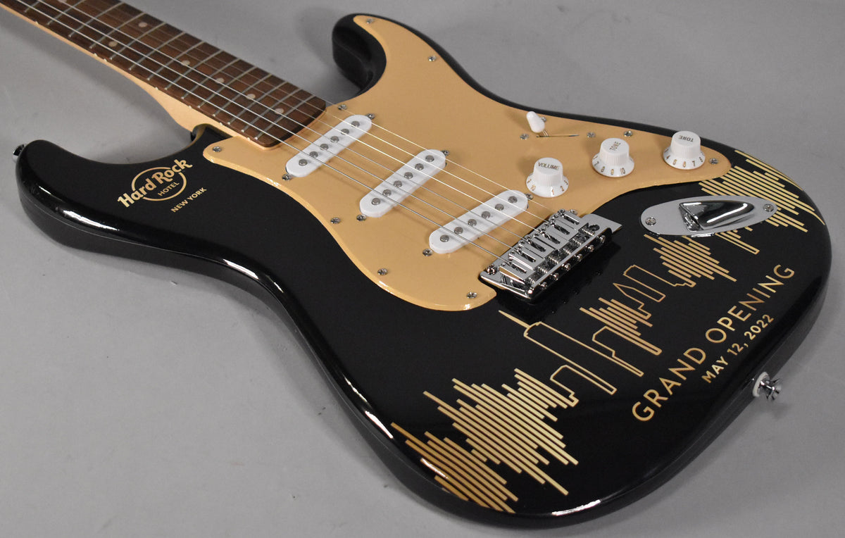 Black Stratocaster with a gold pickguard, white pickups, and a gold Hard Rock Hotel NYC logo and skyline graphic on the body.