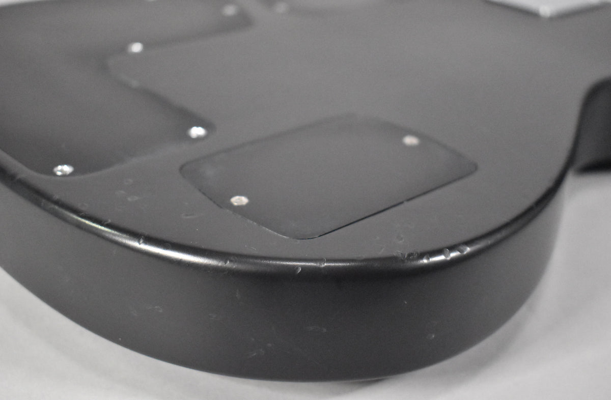 Close-up of the matte black guitar body's lower bout, showing a control cavity cover and several small chips along the edge.