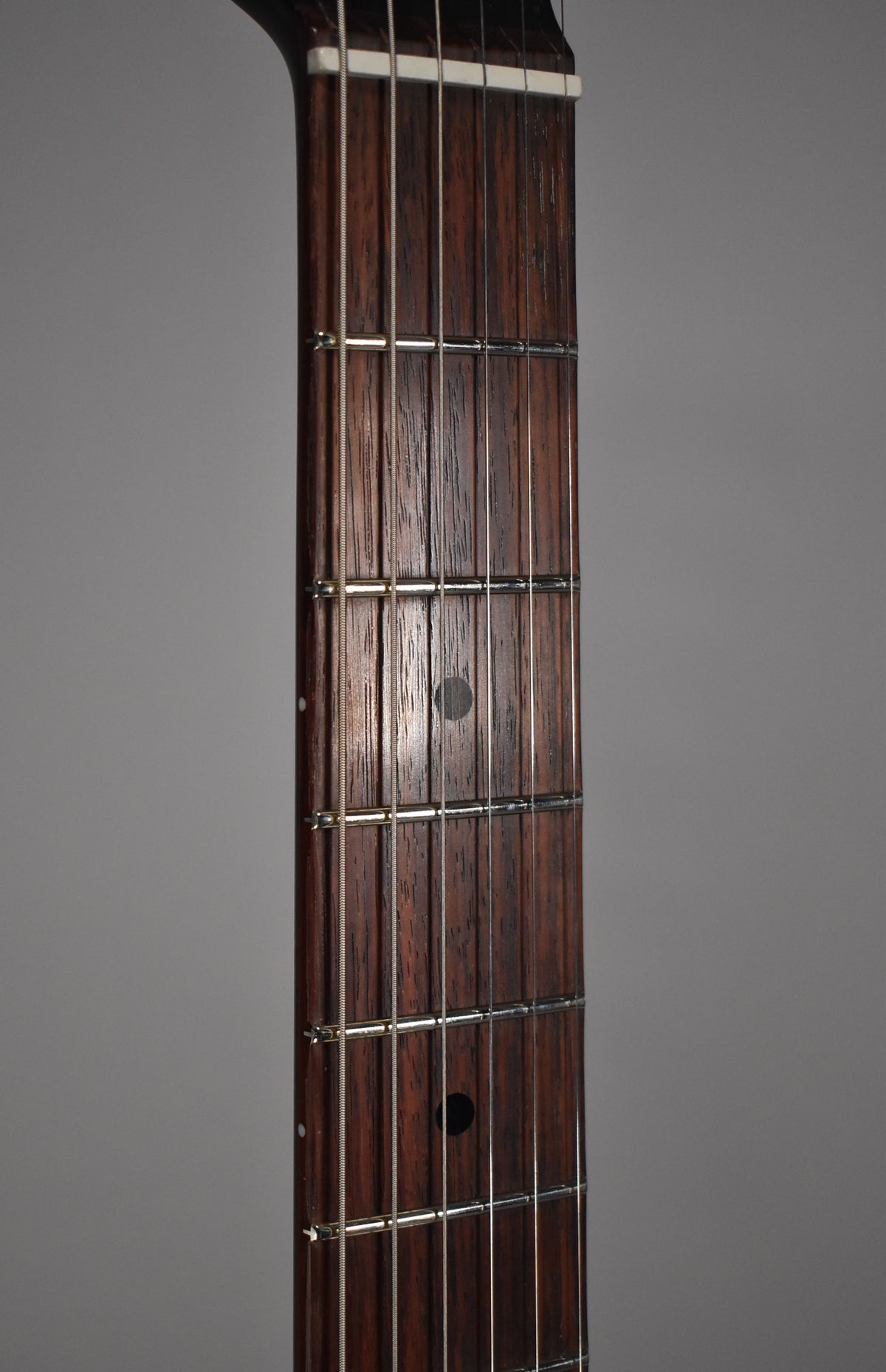 Close-up of the dark rosewood fretboard with a white nut, showing circular fret markers and light wear on the frets.