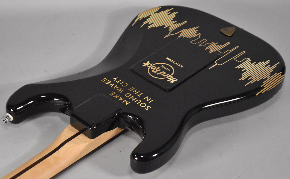 The guitar's glossy black body, viewed from the back, features gold Hard Rock Cafe NYC branding and "MAKE SOUND WAVES IN THE CITY" text.