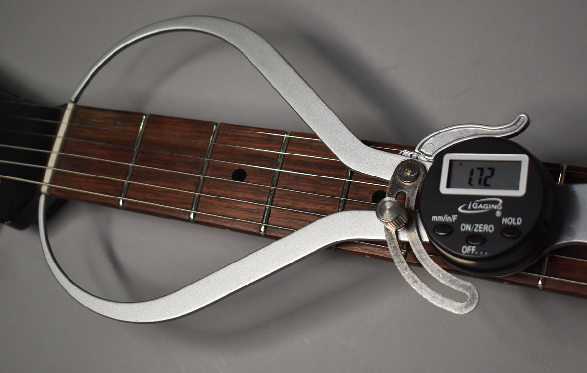 A digital caliper measures the dark brown fretboard, showing a reading of 1.72, with light fret wear visible.