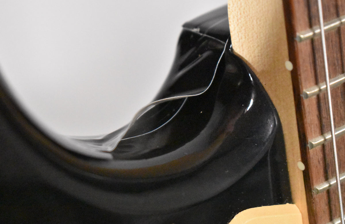 Close-up of the guitar's upper horn and neck joint, showing a clear protective film peeling off the glossy black body.