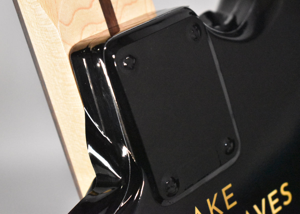 Close-up of the guitar's glossy black body and neck plate, showing the light wood neck and gold lettering on the body.