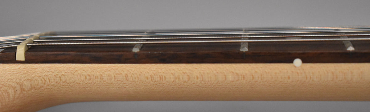 Close-up of the guitar's light wood neck and dark fretboard, showing the nut, strings, frets, and a white side dot marker.