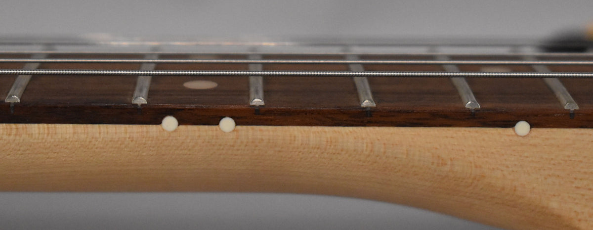Close-up of the guitar's dark rosewood fretboard with white dot inlays and light maple neck, viewed from the side.
