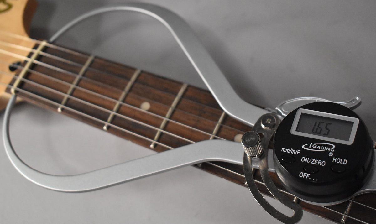 Close-up of the guitar's dark fretboard and frets, with a digital caliper measuring the string height at 1.65.