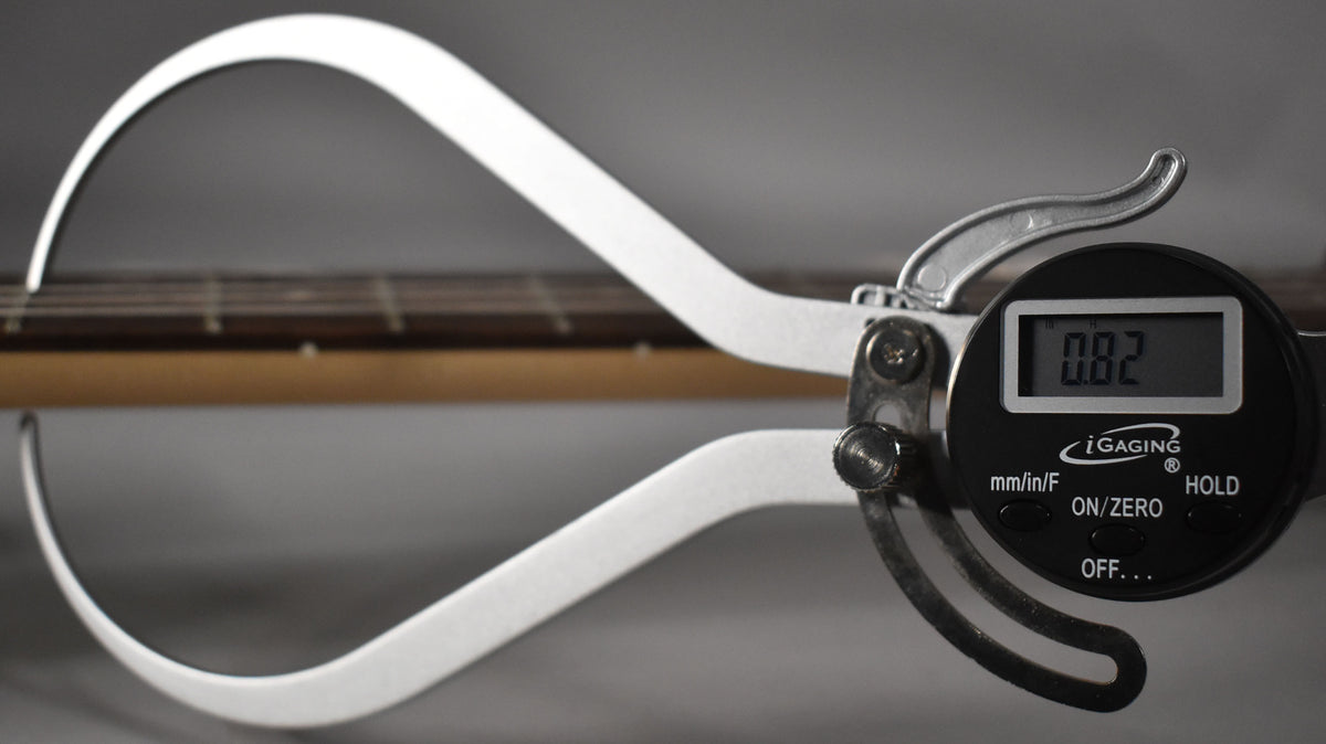 A digital caliper measures the string height above the fretboard, displaying "0.82" on its screen.
