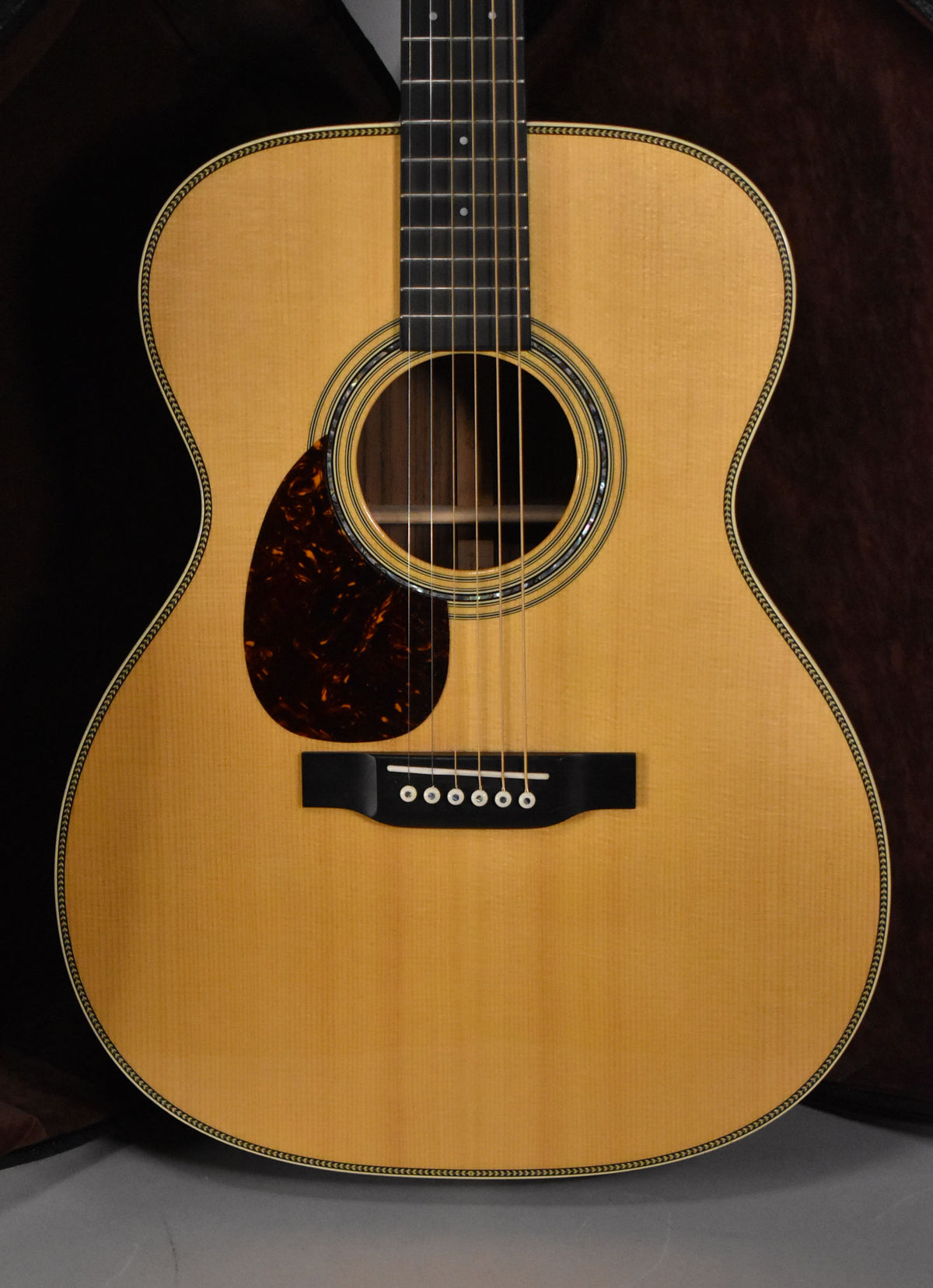 Full front view of the natural finish acoustic guitar, showing the light wood grain, dark pickguard, and ornate soundhole rosette.