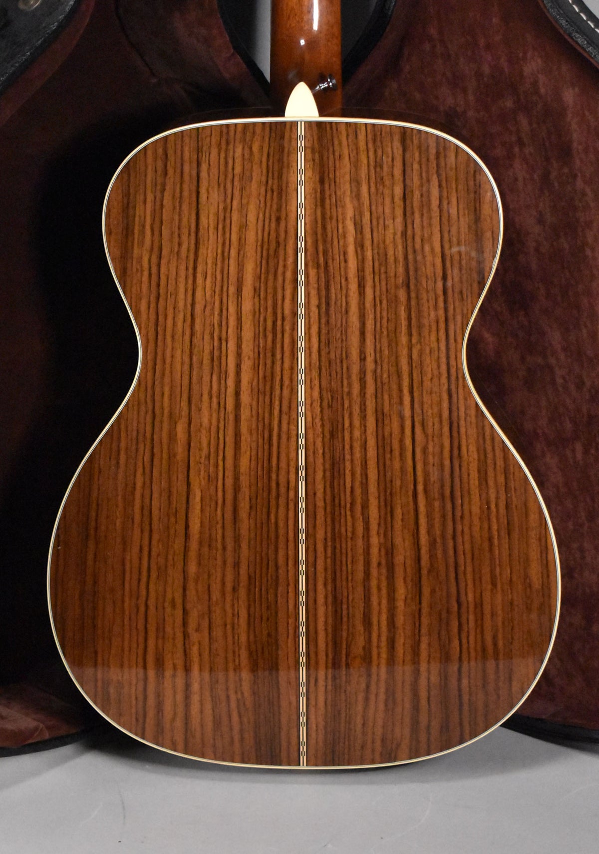 The guitar's back, a glossy dark brown with prominent vertical grain, features a thin white binding and a decorative center strip.