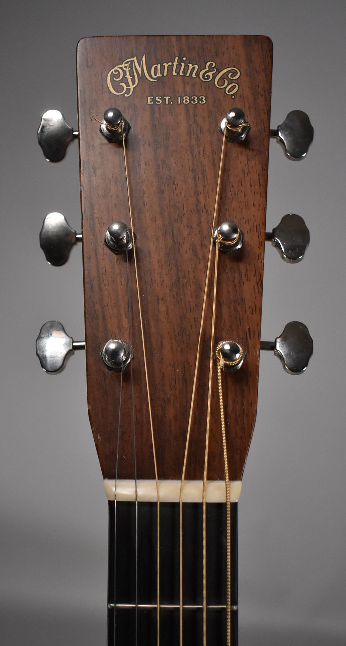 Close-up of the guitar's dark wood headstock, showing six chrome tuners, gold lettering, and the top of the fretboard and nut.