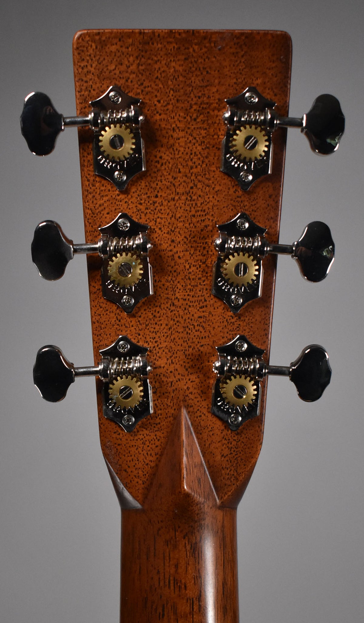 The back of the headstock, showing six open-gear tuners with gold gears and chrome plates, on a natural wood finish.
