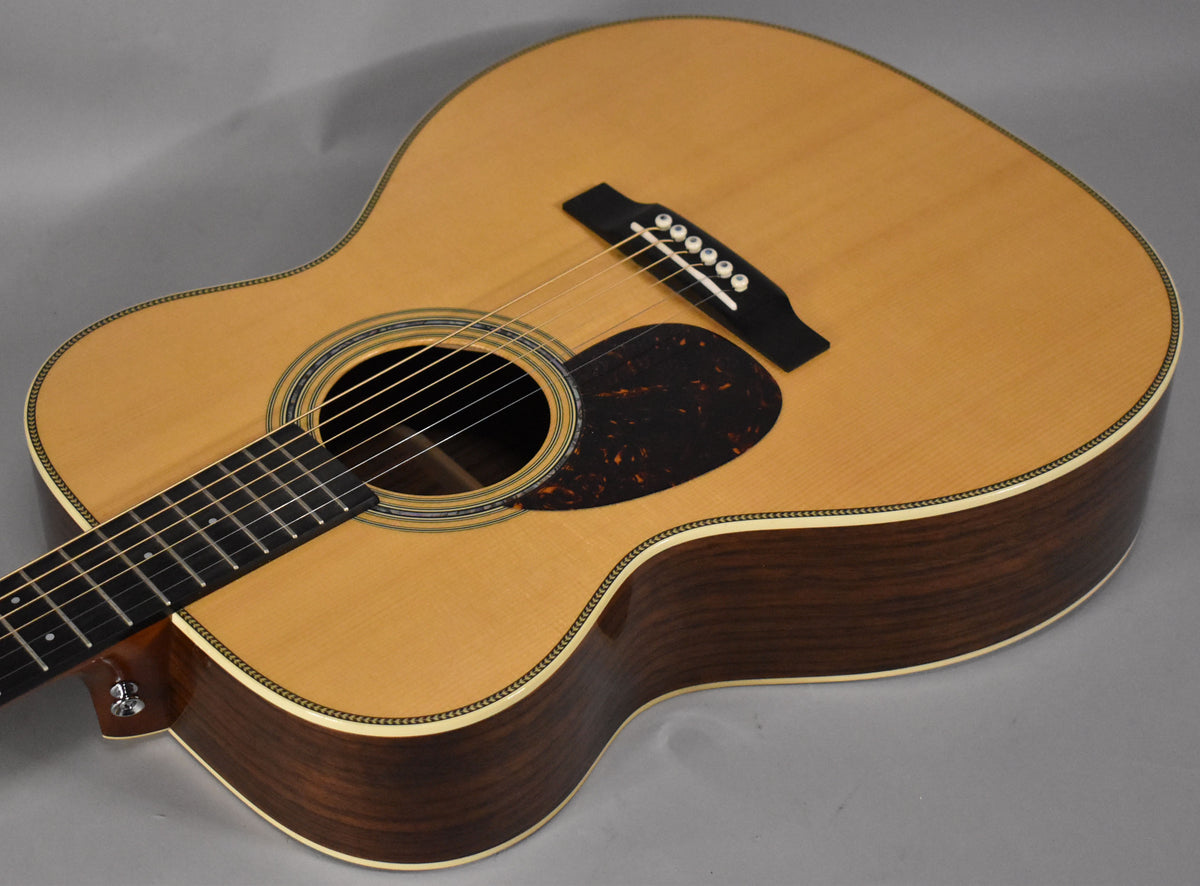 The natural finish acoustic guitar is angled from the upper left, showing the body, soundhole, pickguard, and bridge.