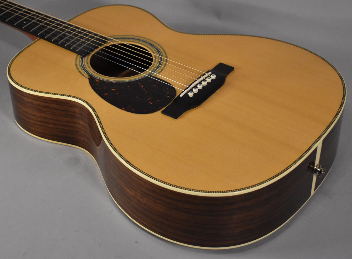 The natural finish acoustic guitar is angled from the upper left, showing its light-colored top, dark sides, and a visible endpin jack.