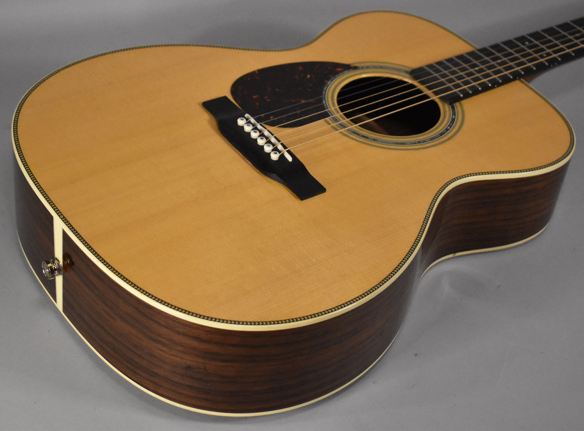 Upper body of a natural finish acoustic guitar, showing the dark wood sides, light top, pickguard, and bridge.