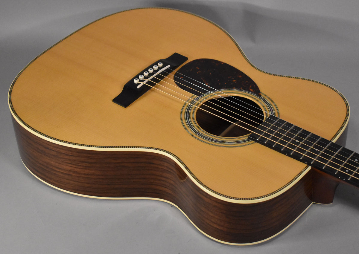 The left-handed acoustic guitar's natural top and dark wood sides are visible from above, showing the soundhole, bridge, and pickguard.