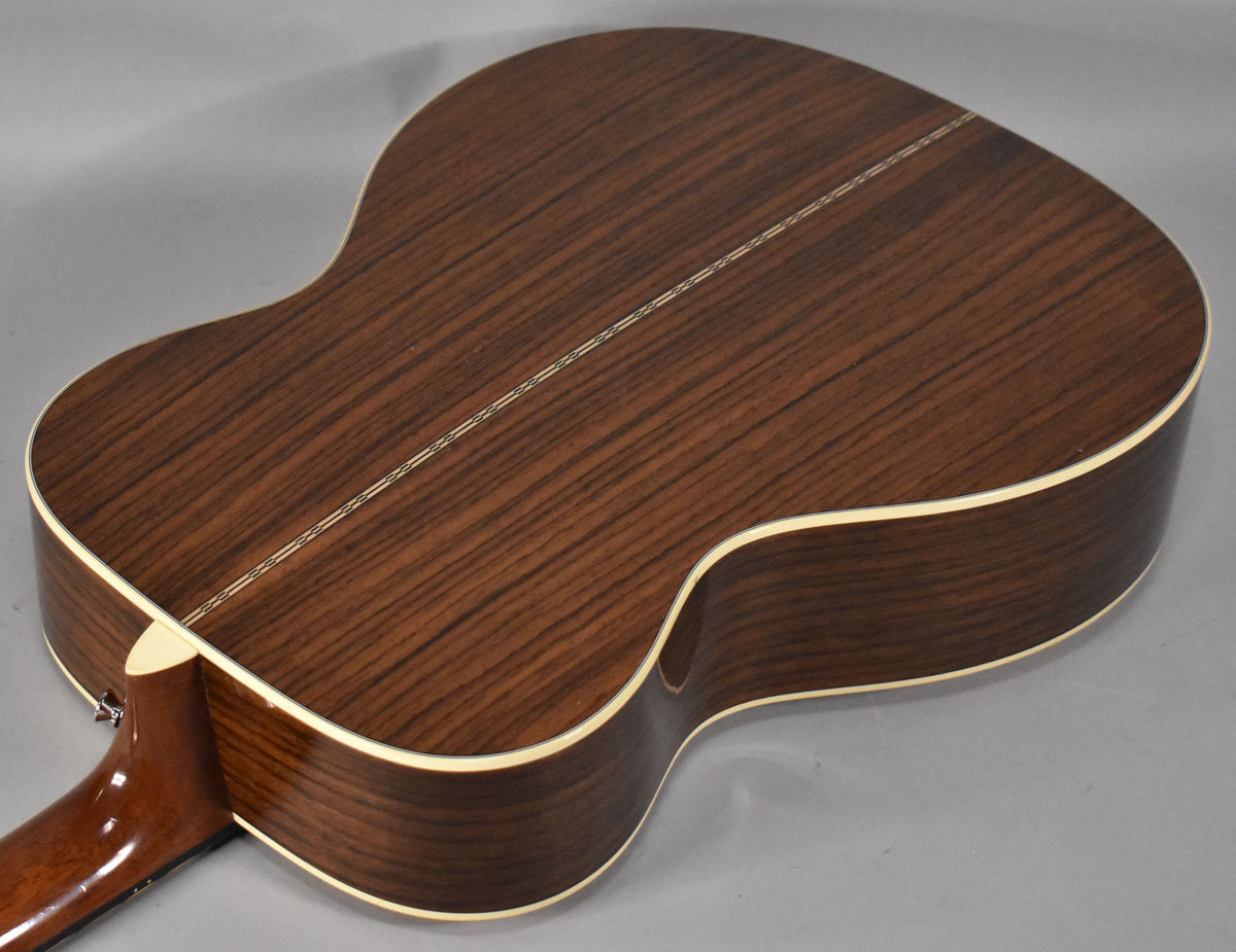 The acoustic guitar's dark brown, glossy back and sides are visible, with a light binding and a decorative stripe down the center.