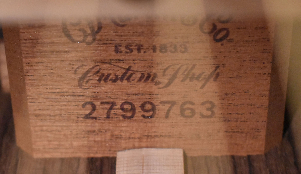 A close-up of the guitar's interior label, showing "Custom Shop" and a serial number "2799763" stamped on light brown wood.