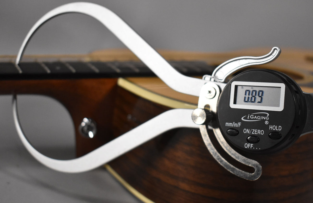 A digital caliper measures the guitar's dark brown neck, showing a 0.89mm reading on its black display.