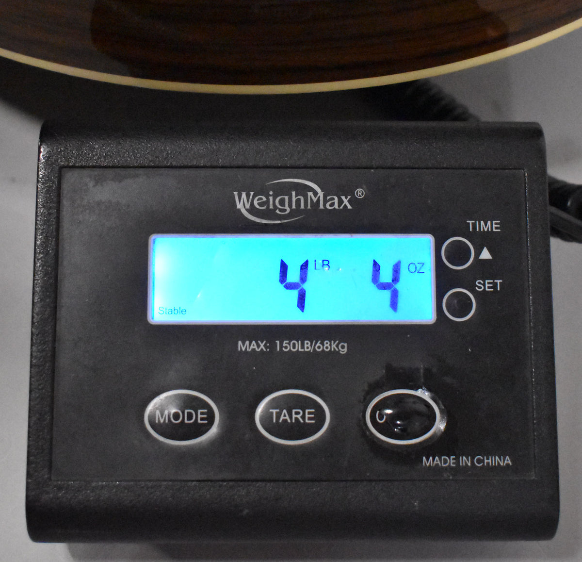 A black digital scale displays "4 LB 4 OZ" in bright blue, with a dark wood guitar body visible at the top.