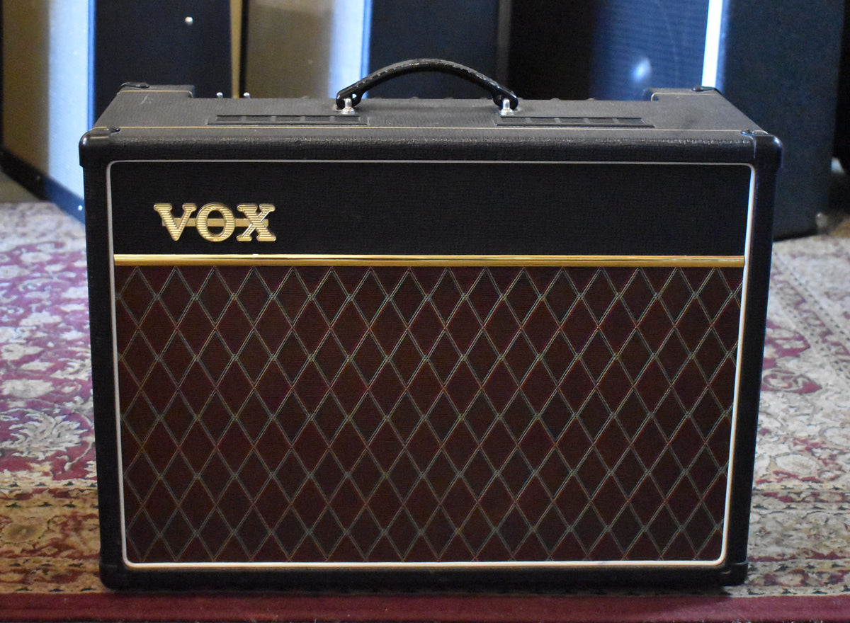 Front view of a black combo amp with a dark red diamond-patterned grille, gold trim, and a black leather handle on top.