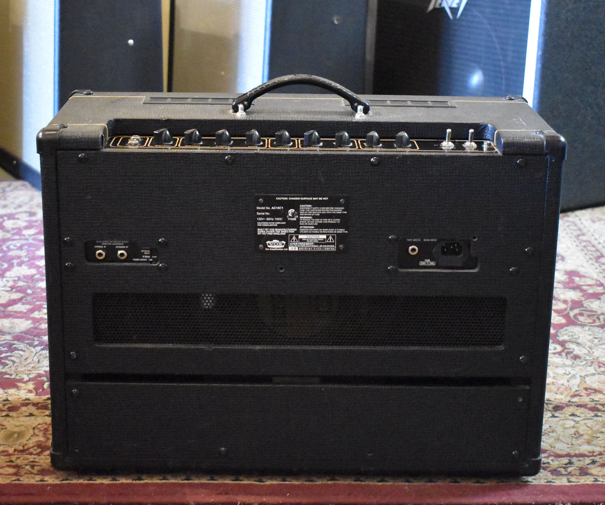 Rear view of a black textured combo amp, showing the control panel with black knobs and two toggle switches, and various input/output jacks.