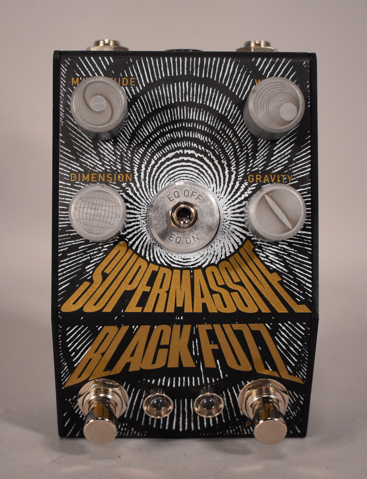 Black fuzz pedal with gold lettering and white radiating lines, featuring four clear dome knobs and a central EQ toggle switch.