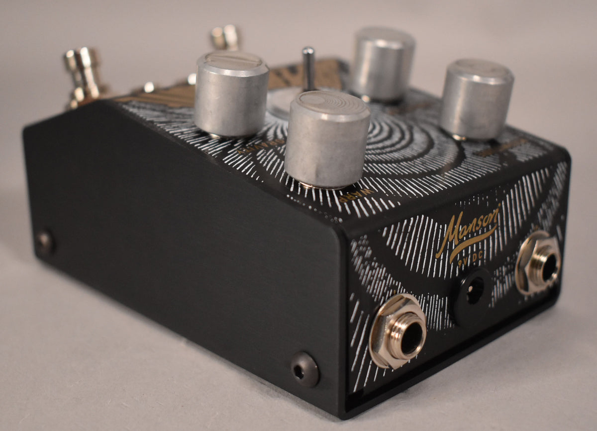 The black pedal, angled from the right, has a silver and gold spiral design, four silver knobs, and two input jacks.