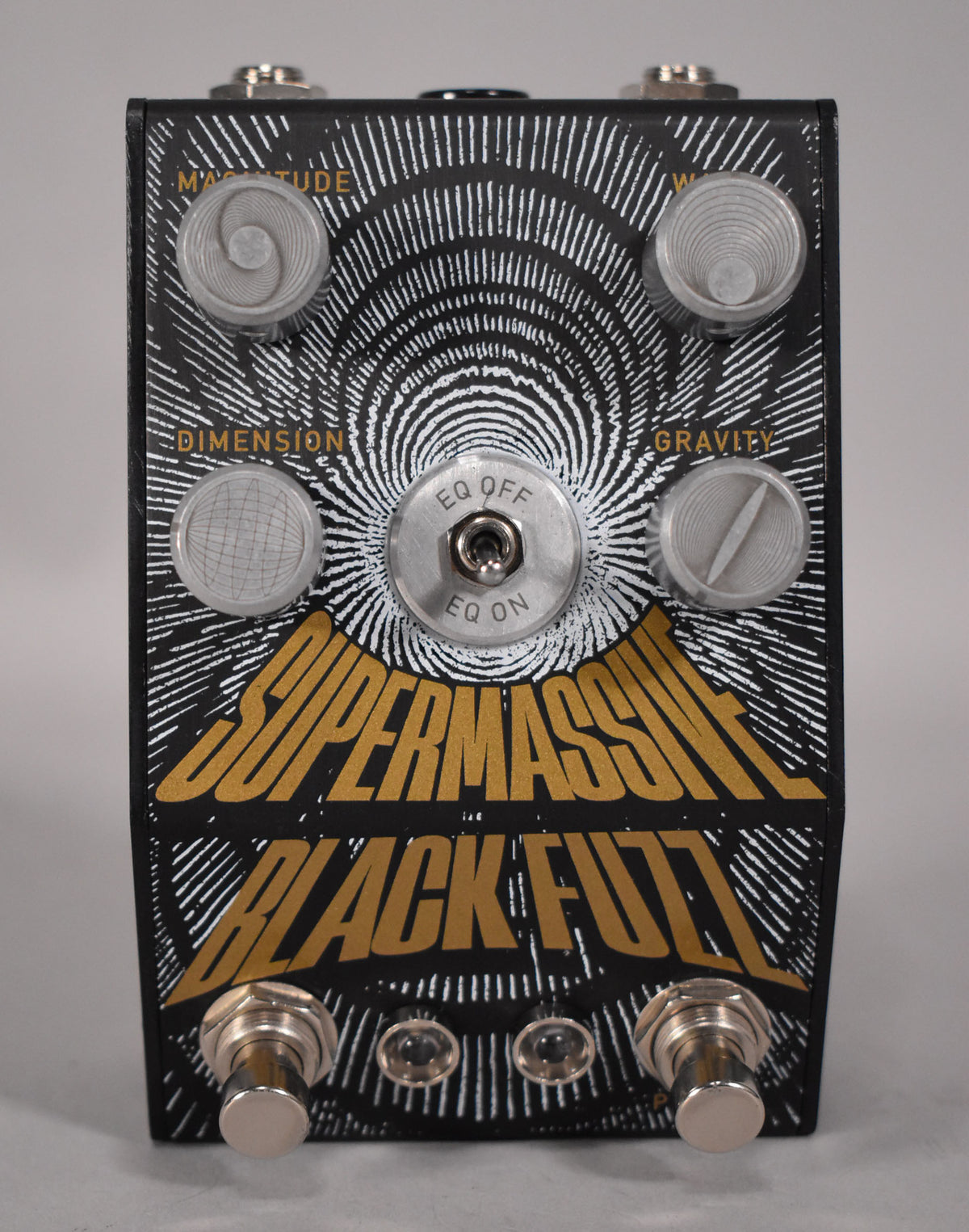 A black fuzz pedal with a gold and white graphic, four textured silver knobs, a silver EQ toggle switch, and two silver footswitches.