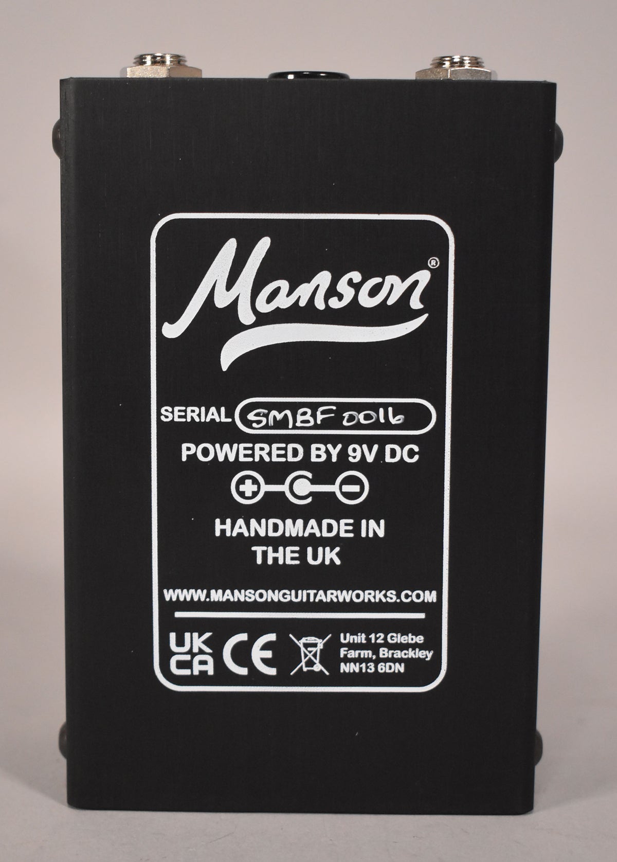 The black pedal's back panel is centered, showing white text for serial number SMBF 0016, power, and UK manufacturing details.