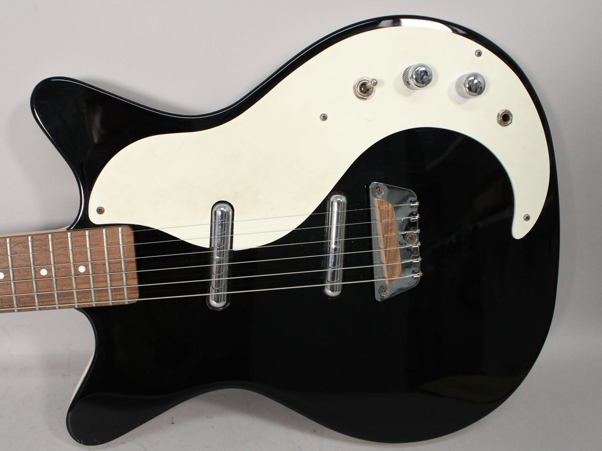 Close-up of the glossy black body and cream pickguard, showing two lipstick pickups, a wooden bridge, and three chrome knobs.