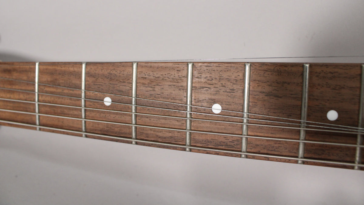 Close-up of the guitar's dark brown fretboard with silver frets and white dot inlays, viewed from the bass side.