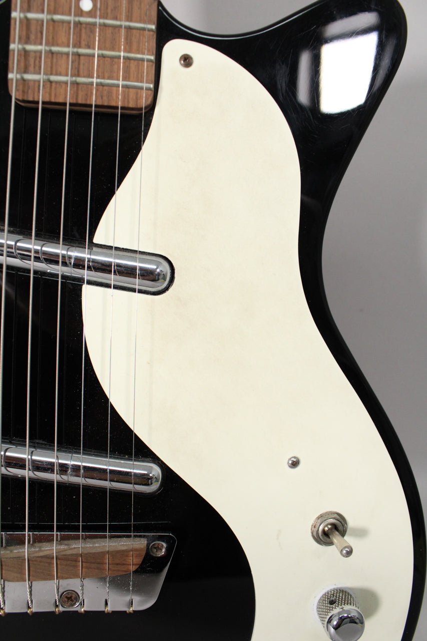 Close-up of a black gloss guitar body with a cream pickguard, showing two chrome lipstick pickups, a bridge, and a toggle switch.