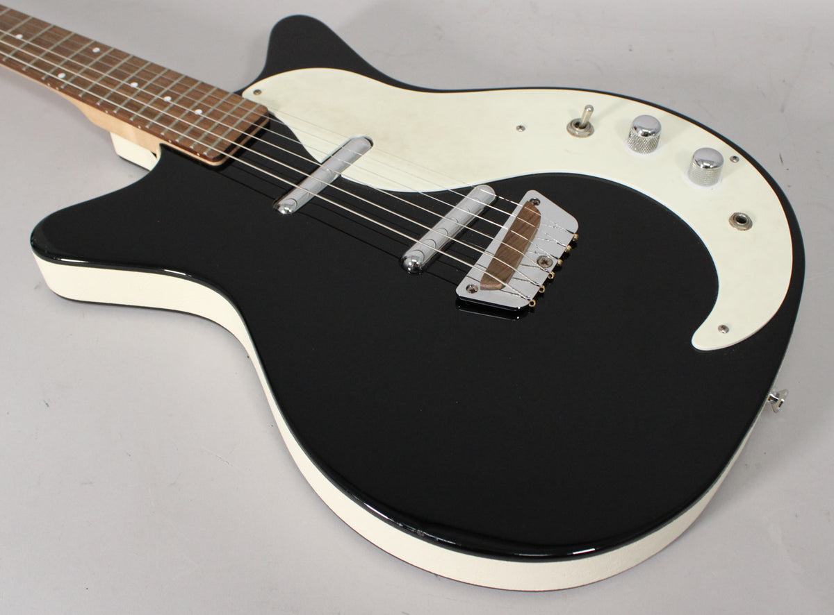 The black gloss guitar body, with white binding and pickguard, is angled from the neck to show the bridge and controls.
