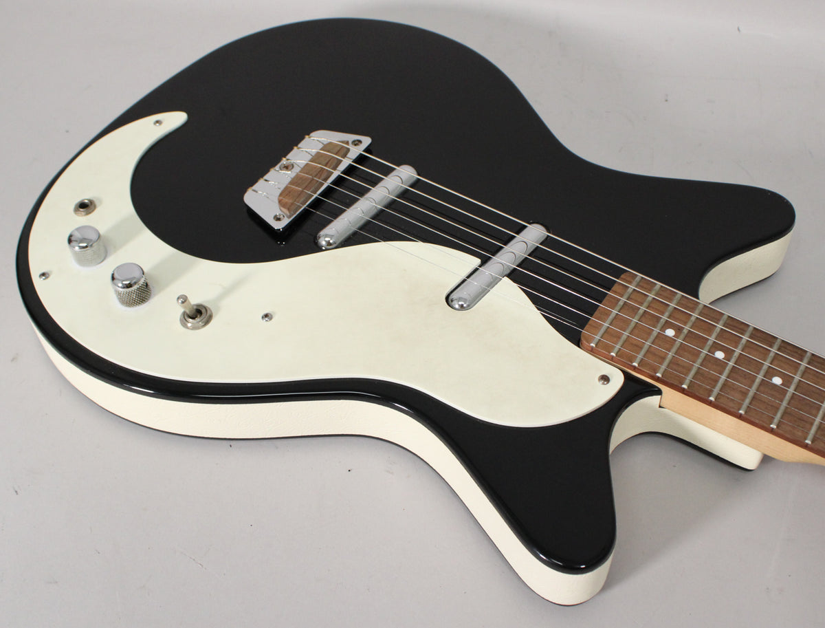 Black gloss electric guitar, angled from above, showing the body, white pickguard, two chrome knobs, and a toggle switch.