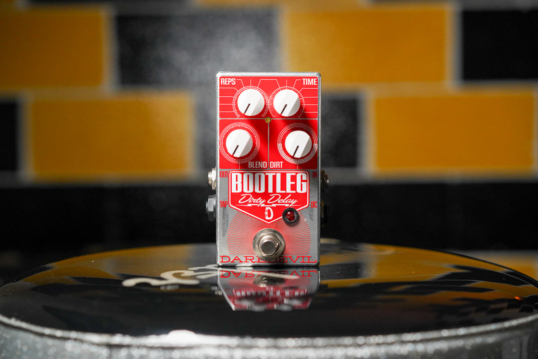 A top-down view of a silver and red pedal with four white knobs, a footswitch, and a red LED.