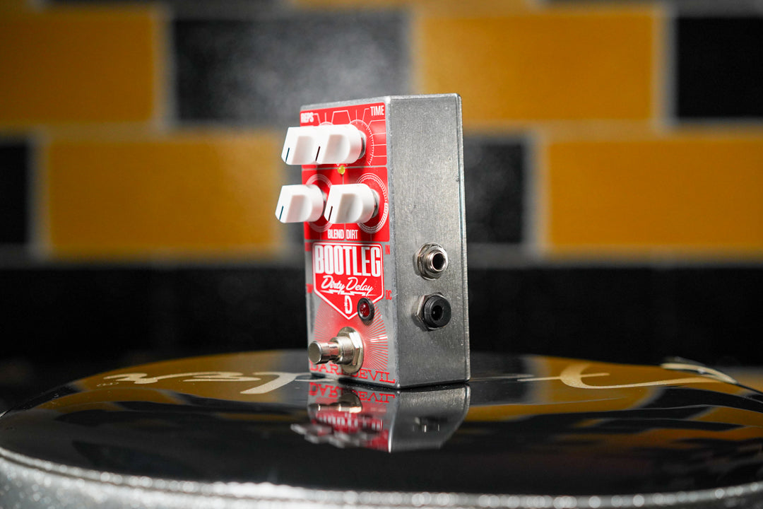 The red and silver delay pedal is angled slightly right, showing its three white knobs, footswitch, and two input jacks.