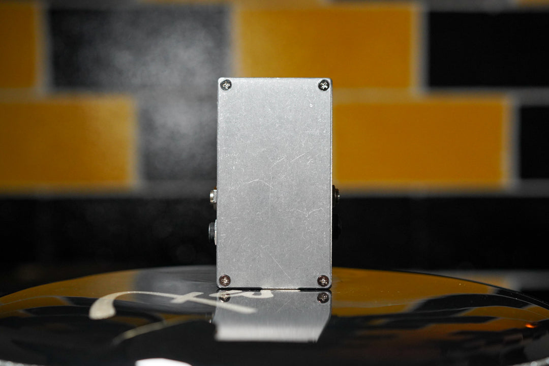 The silver-grey pedal is viewed from the side, showing two input jacks and light surface scratches on its brushed finish.
