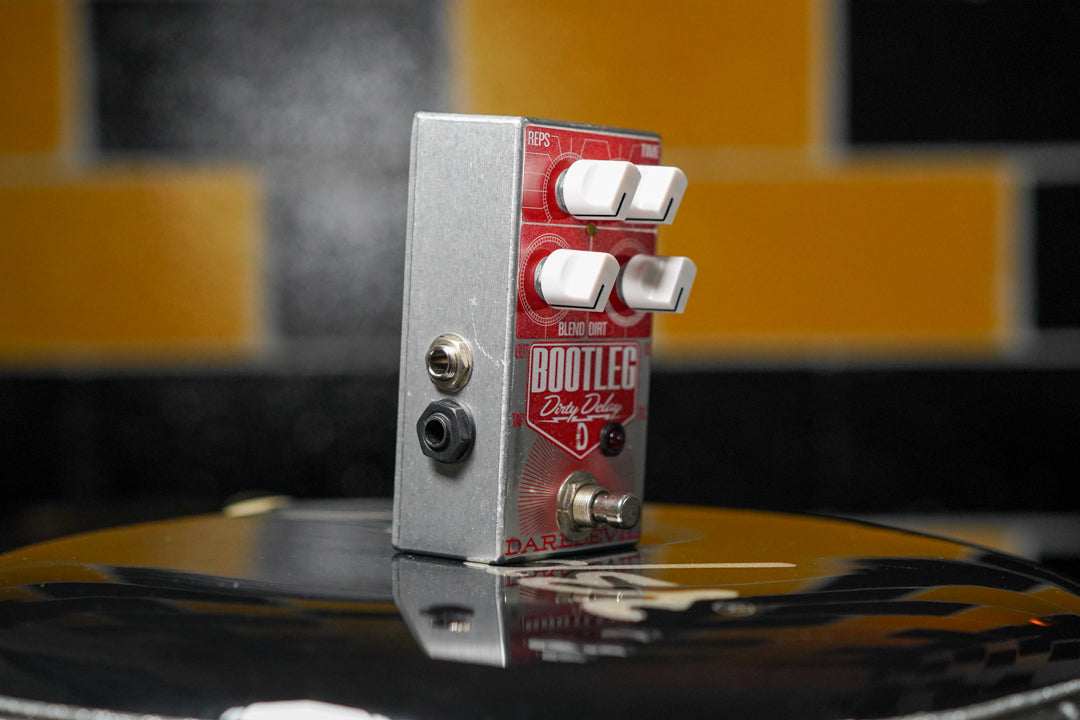 The silver-sided pedal with a red faceplate is angled to show its input jacks and four white control knobs.