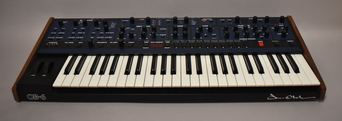 A dark blue synthesizer with a 49-key keyboard, pitch and mod wheels, and wood end cheeks, viewed from a slight angle.