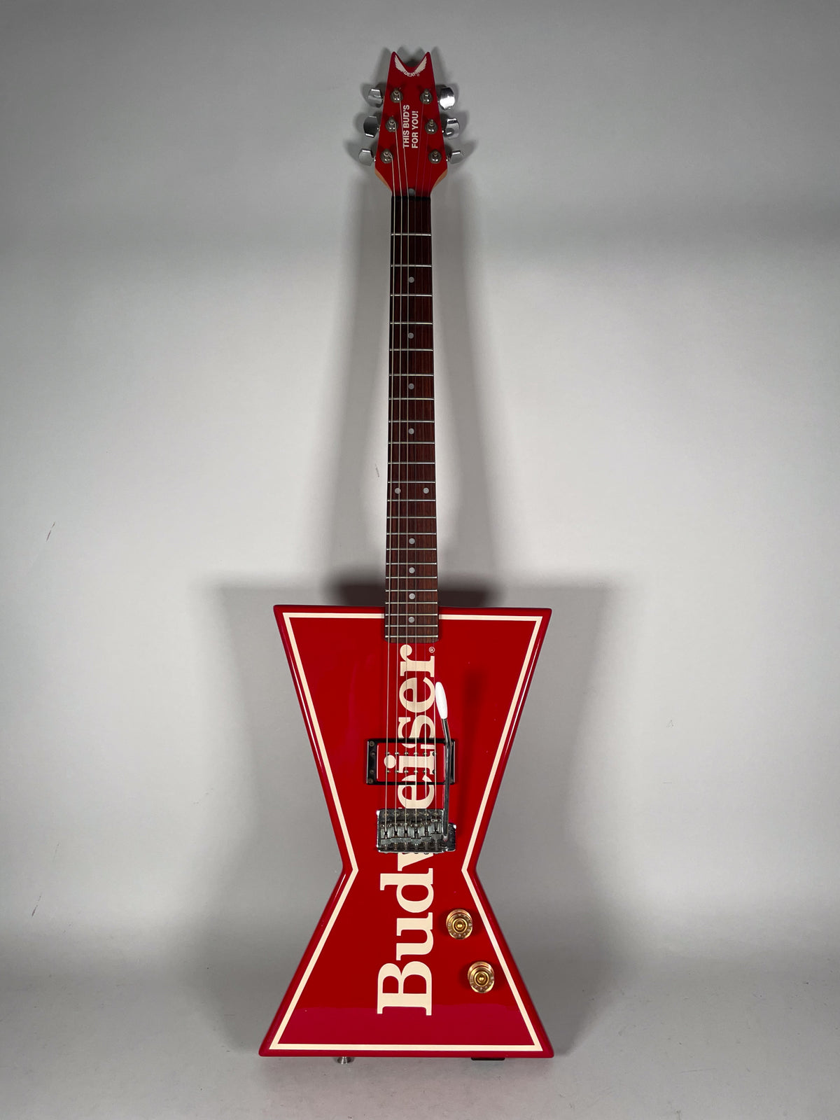 Full front view of a red bowtie-shaped guitar with white trim, a Floyd Rose tremolo, and two gold control knobs.