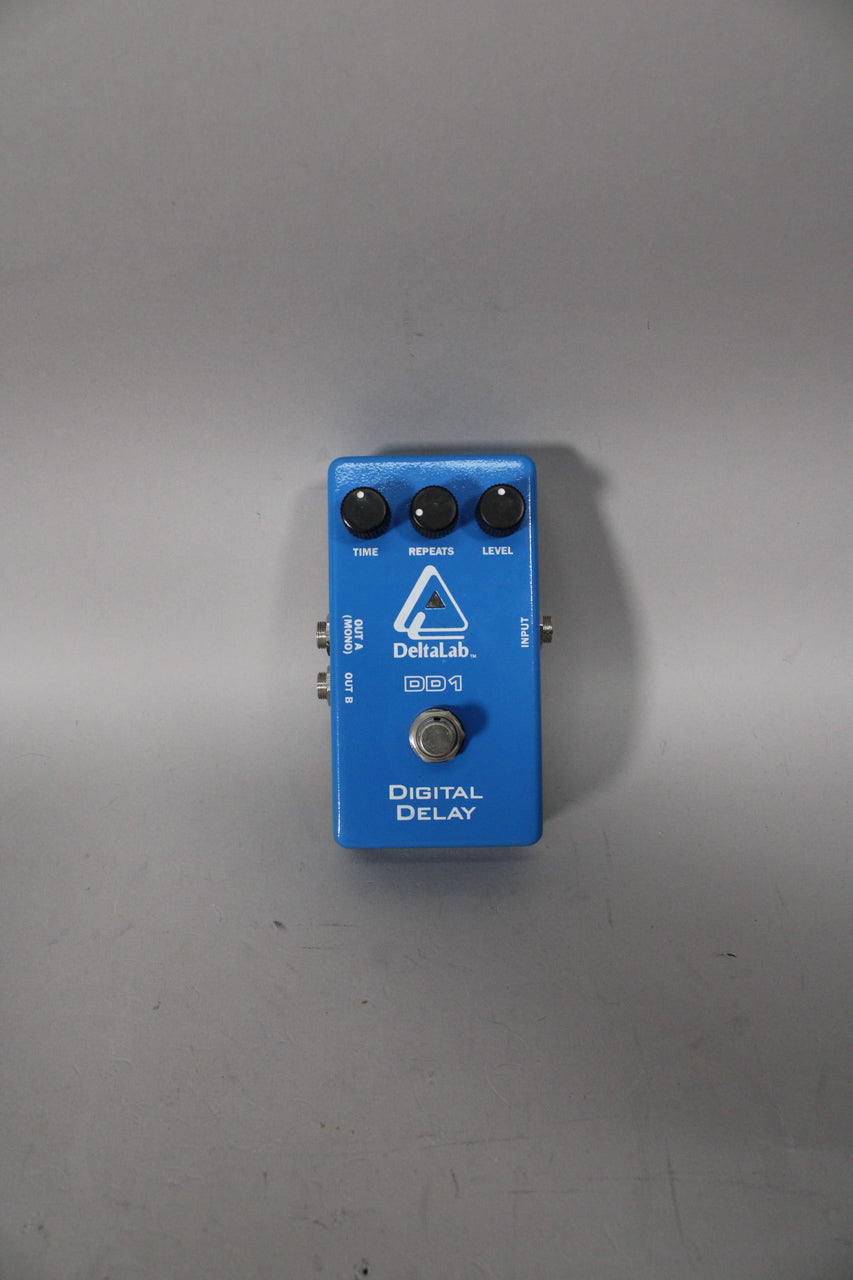 A top-down view of a rectangular blue pedal with three black control knobs, a silver footswitch, and three input/output jacks.