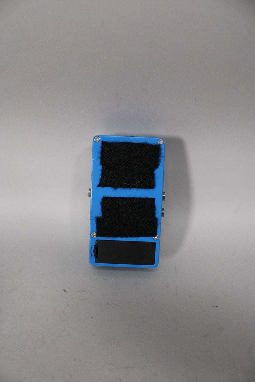 The pedal's bright blue underside is visible, with two large strips of black hook-and-loop tape and a black battery compartment.