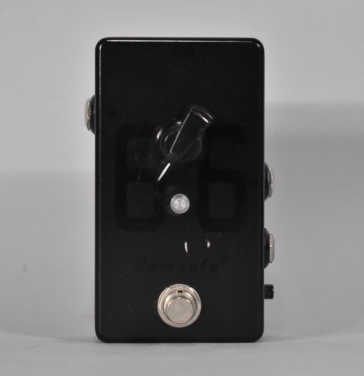 A black rectangular pedal with a large chrome footswitch, a clear toggle switch, and a small white LED on its face.