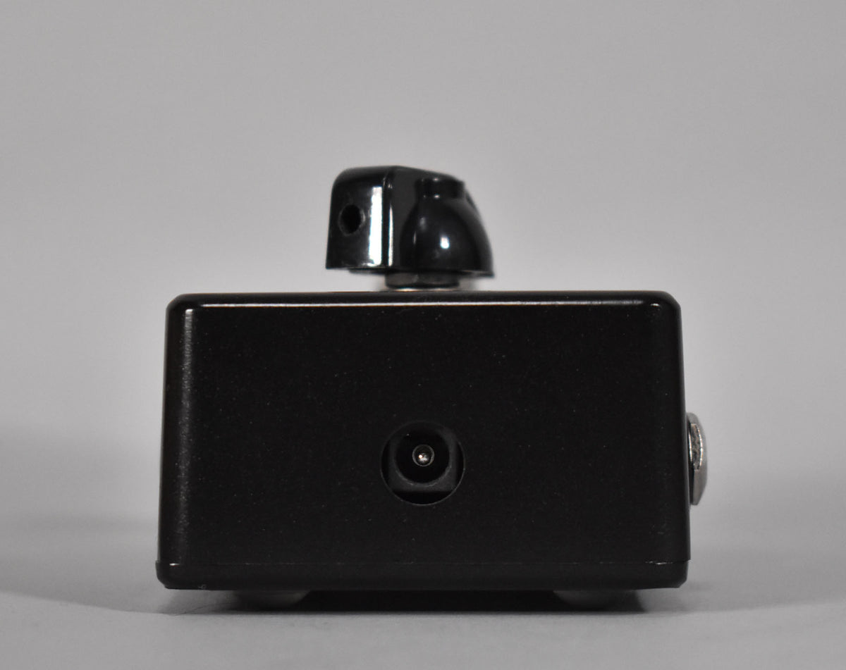 The black boost pedal is viewed from the side, showing a power input jack and a single black control knob on top.