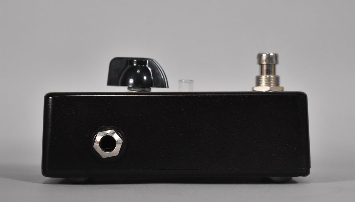 The boost pedal is shown from the left side, revealing a black textured finish, a silver input jack, and a black control knob.