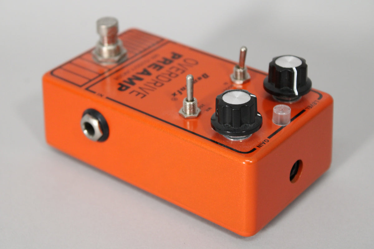 Orange pedal, angled from the left, showing the input jack, footswitch, two toggle switches, and two black control knobs.