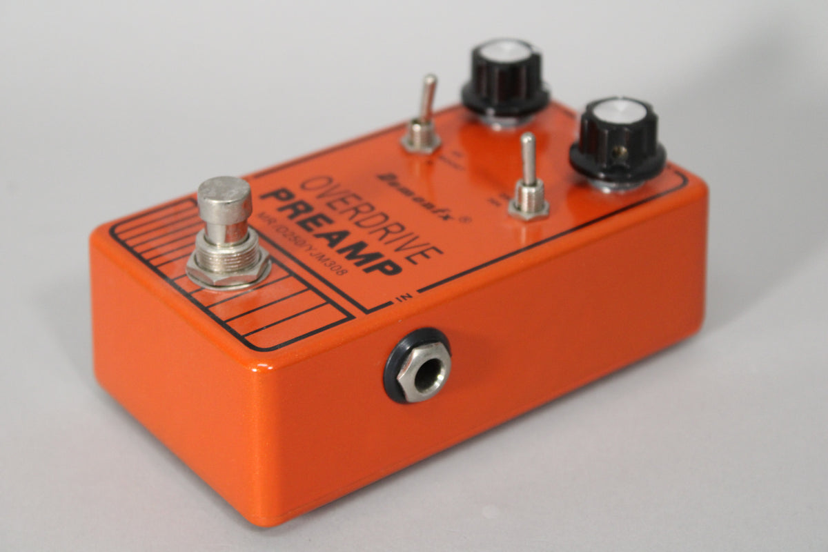An orange metallic pedal, viewed from the front right, with a footswitch, two toggle switches, two black knobs, and an input jack.