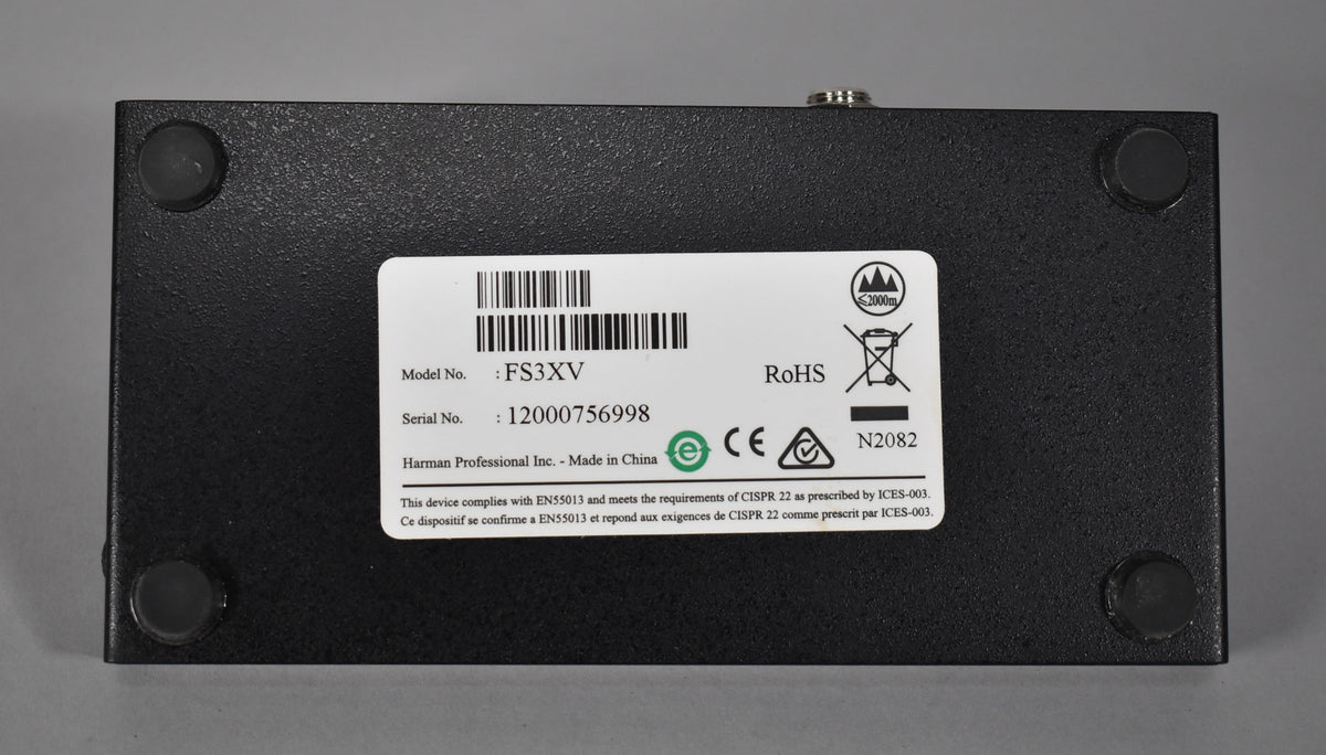 The footswitch's textured black metal underside, with four rubber feet and a white product information sticker, is shown from above.